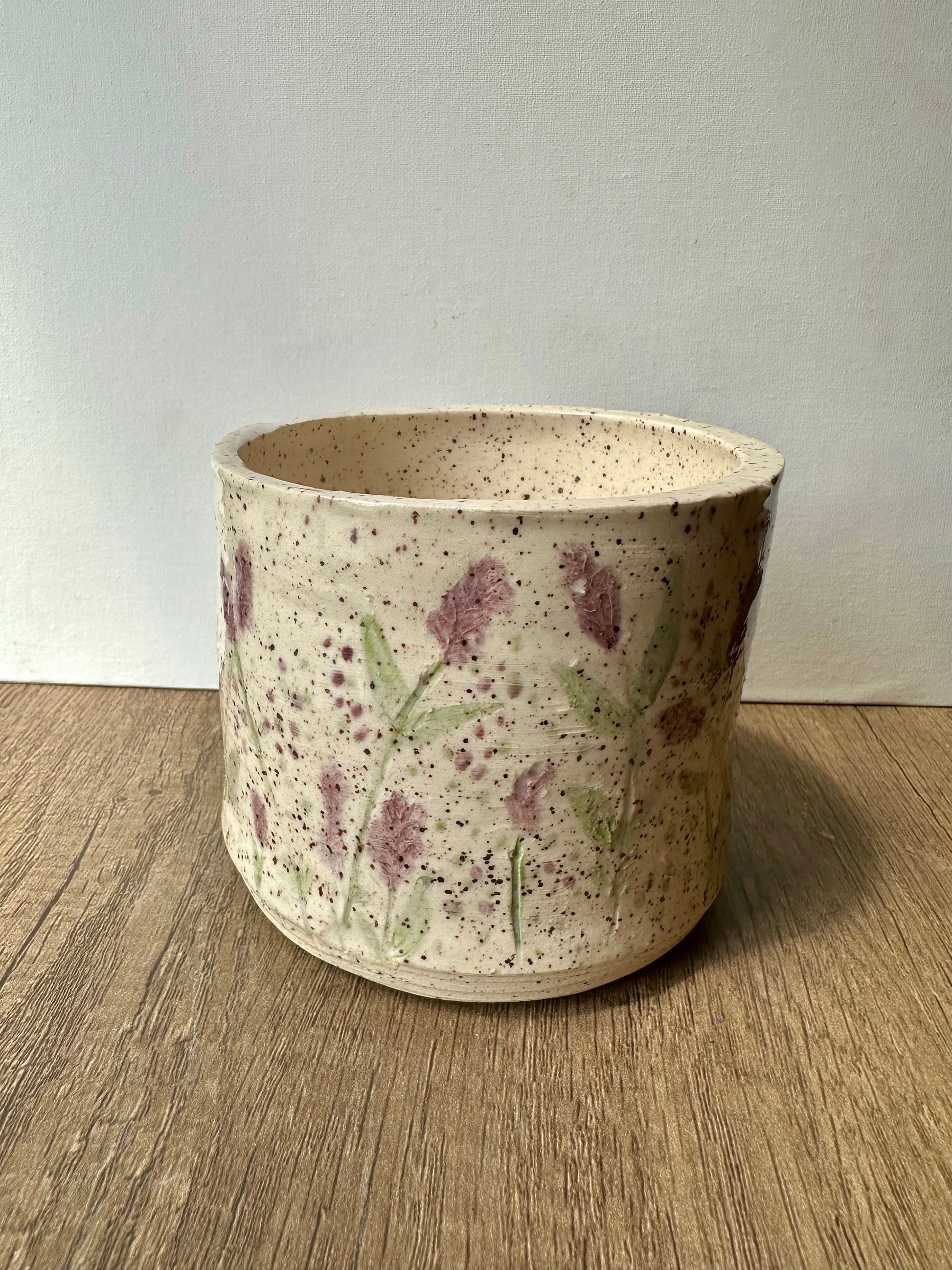 A speckled white clay cylinder with pressed and painted lavender stems, and purple and green polka dots.