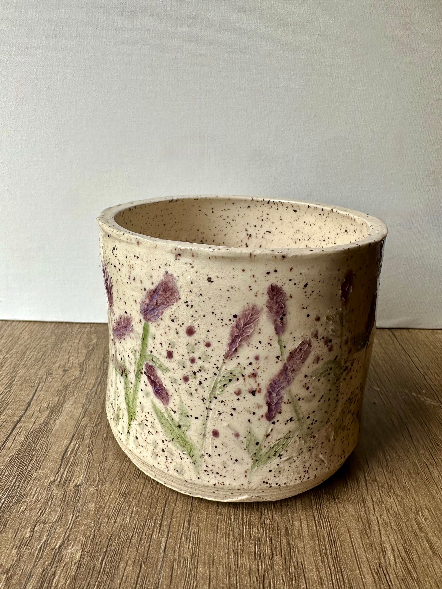 A speckled white clay cylinder with pressed and painted lavender stems, and purple and green polka dots.