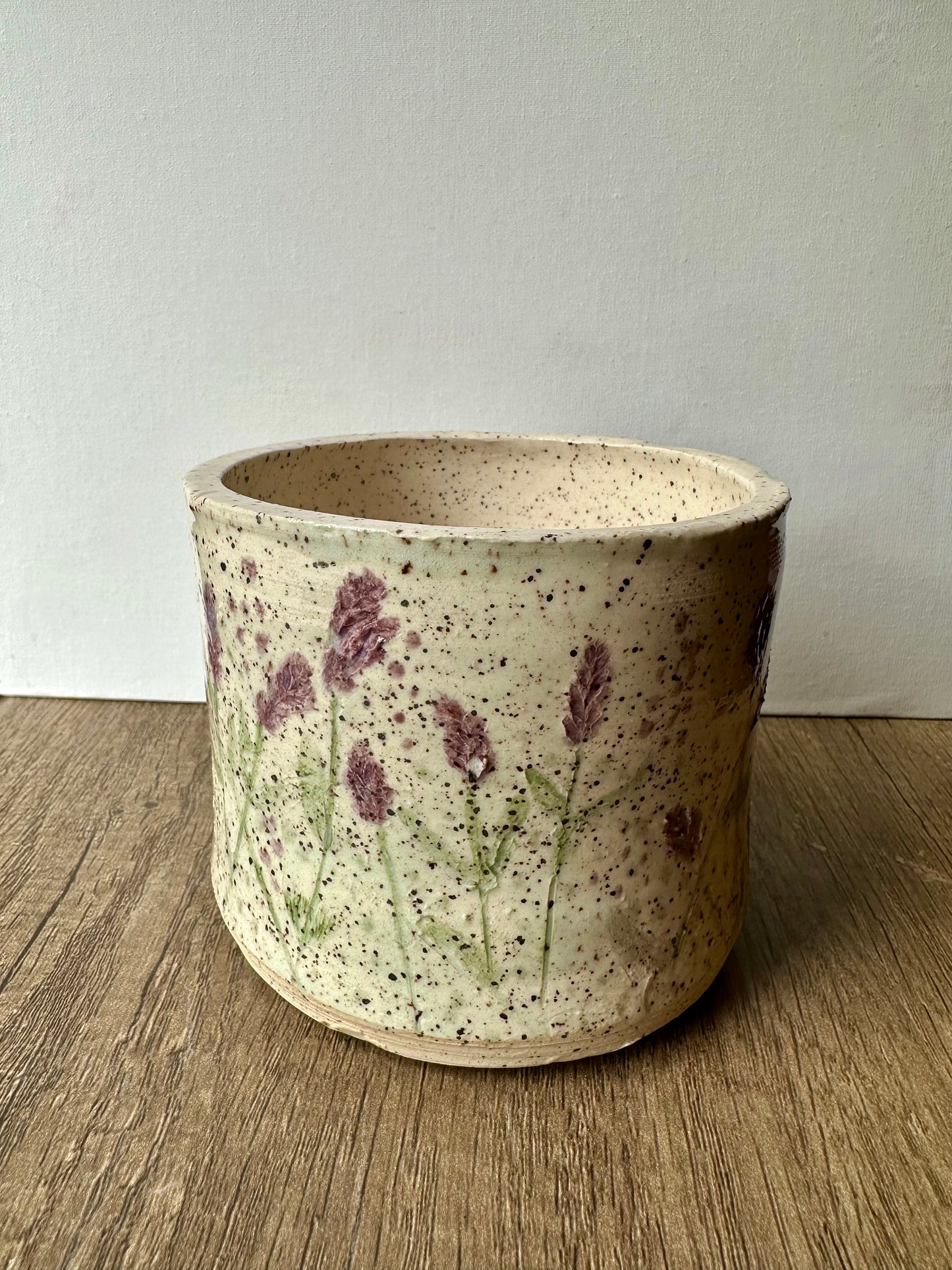 A speckled white clay cylinder with pressed and painted lavender stems, and purple and green polka dots.