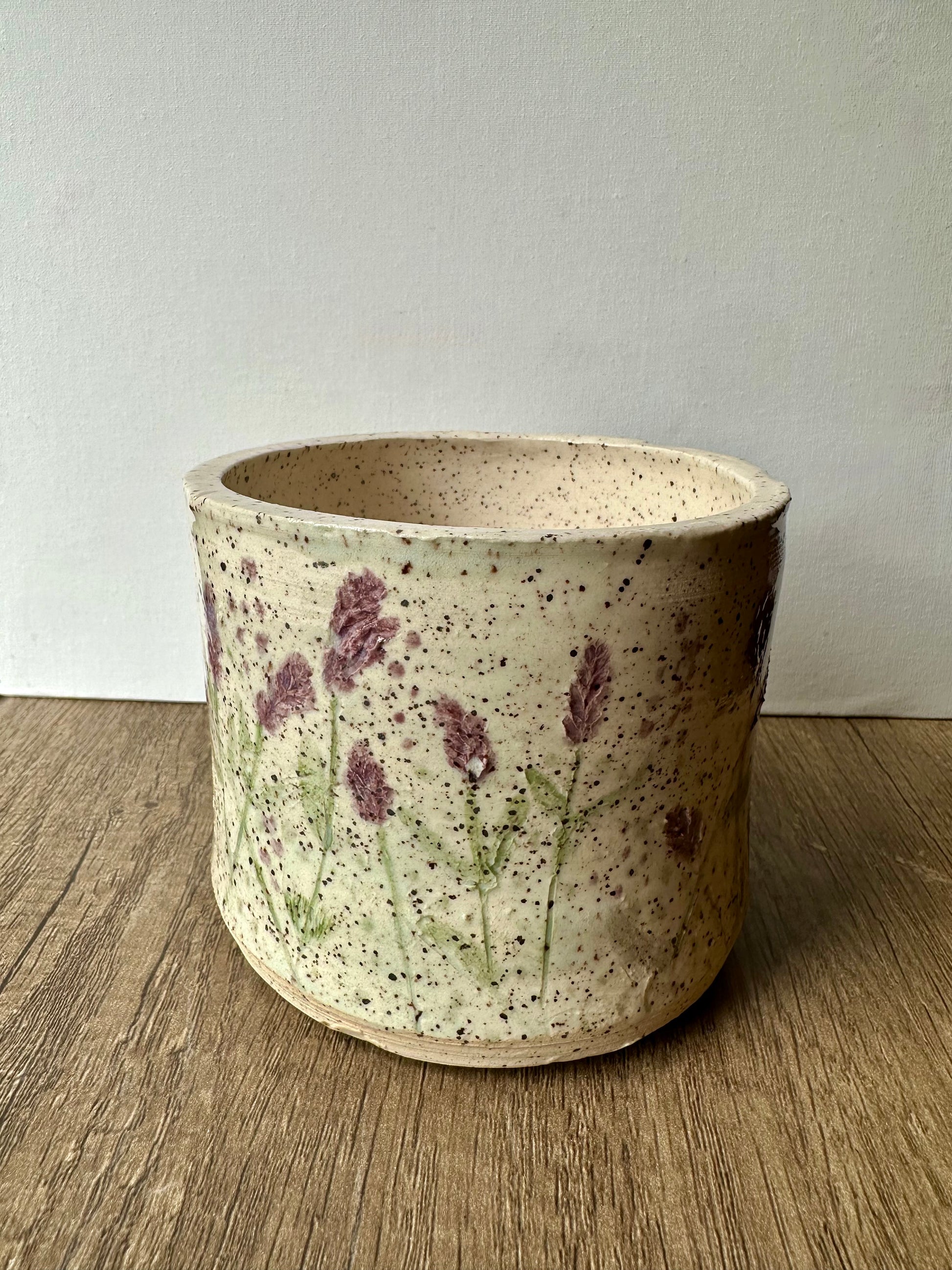A speckled white clay cylinder with pressed and painted lavender stems, and purple and green polka dots.