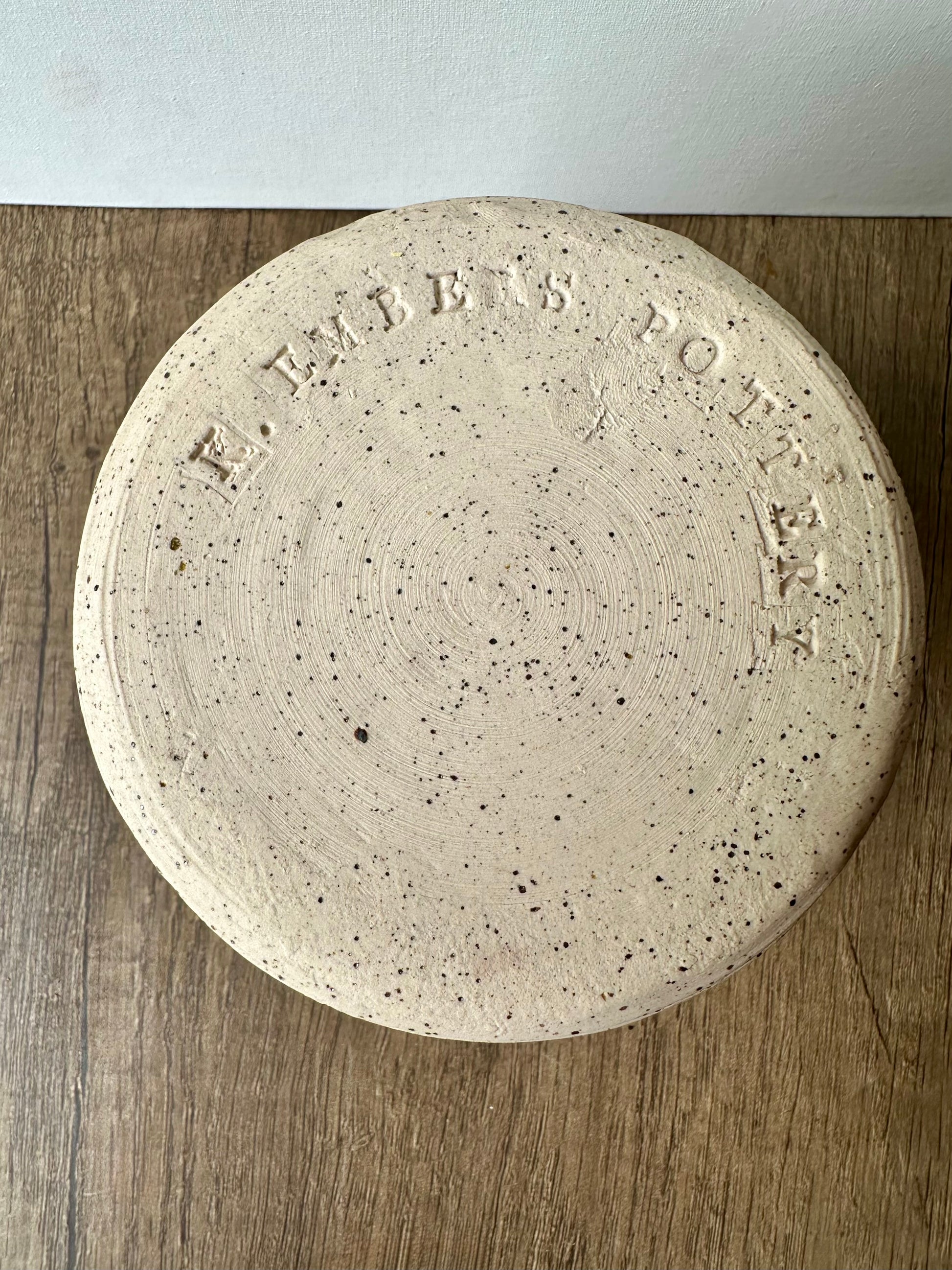 The unglazed bottom of the white ceramic vessel with black speckles; "K. Embers Pottery" stamped in.