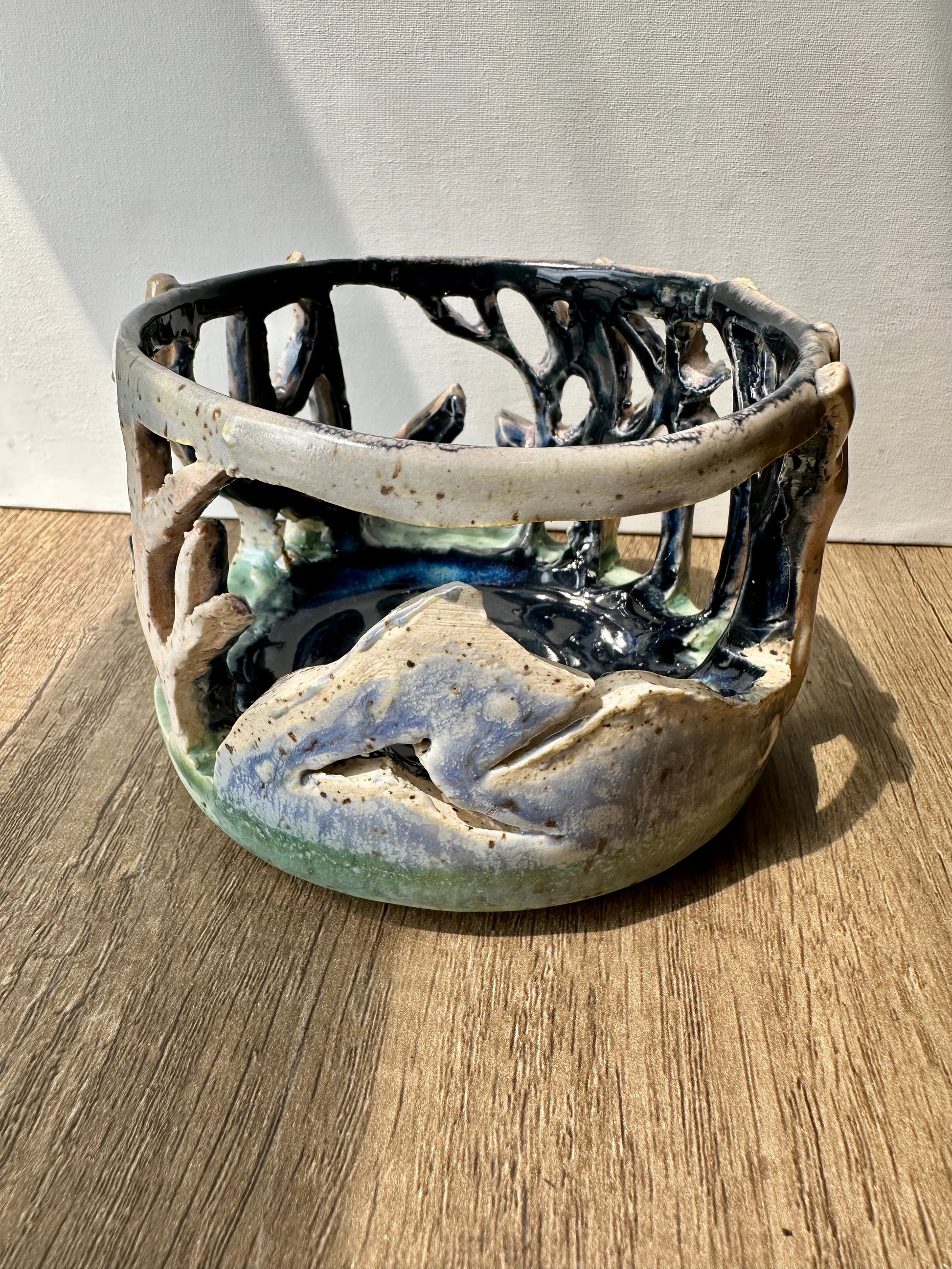Round ceramic candle surround with mountain and birch trees cut out.