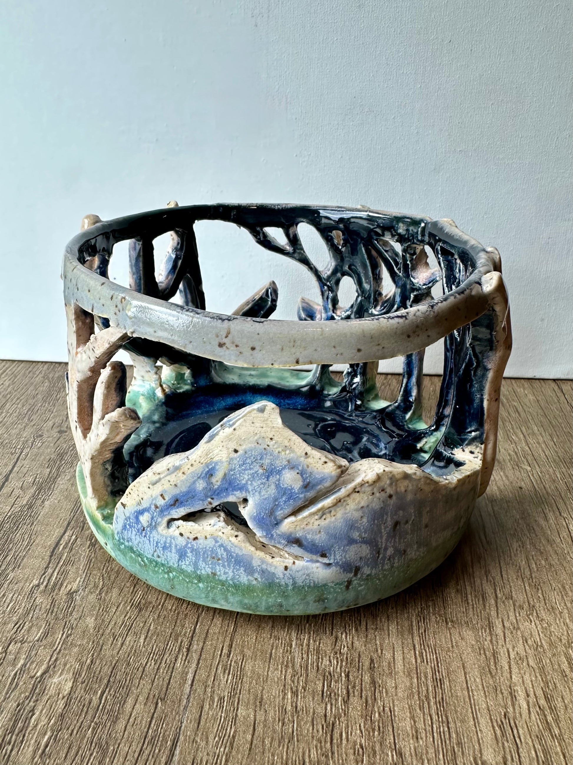 Round ceramic candle surround with mountain and birch trees cut out.