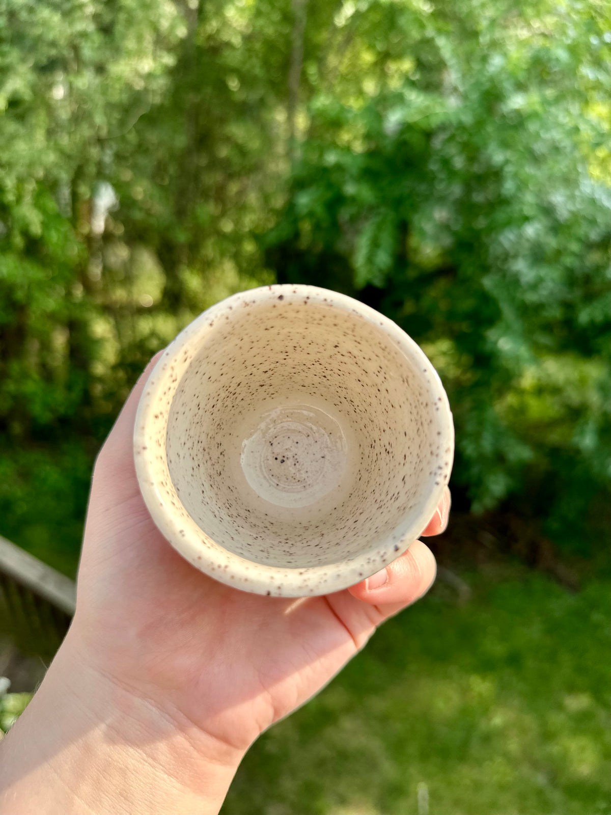 A hold holds and shows the interior of a speckled white ceramic cup.