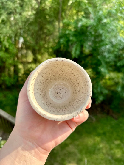 A hold holds and shows the interior of a speckled white ceramic cup.