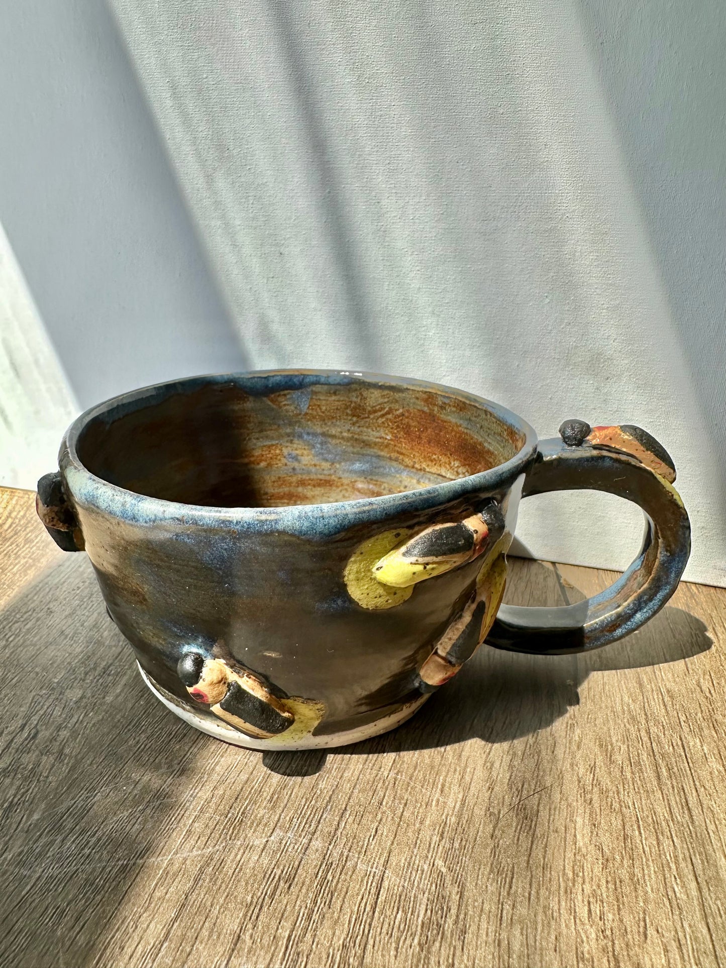 Bronze-colored mug with streaks of inky blue and sculpted fireflies.