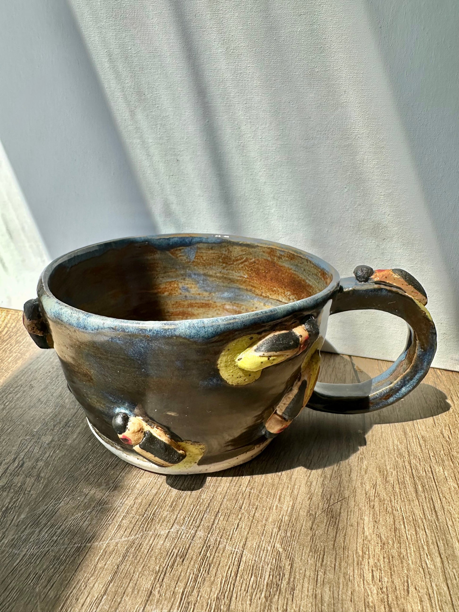 Bronze-colored mug with streaks of inky blue and sculpted fireflies.