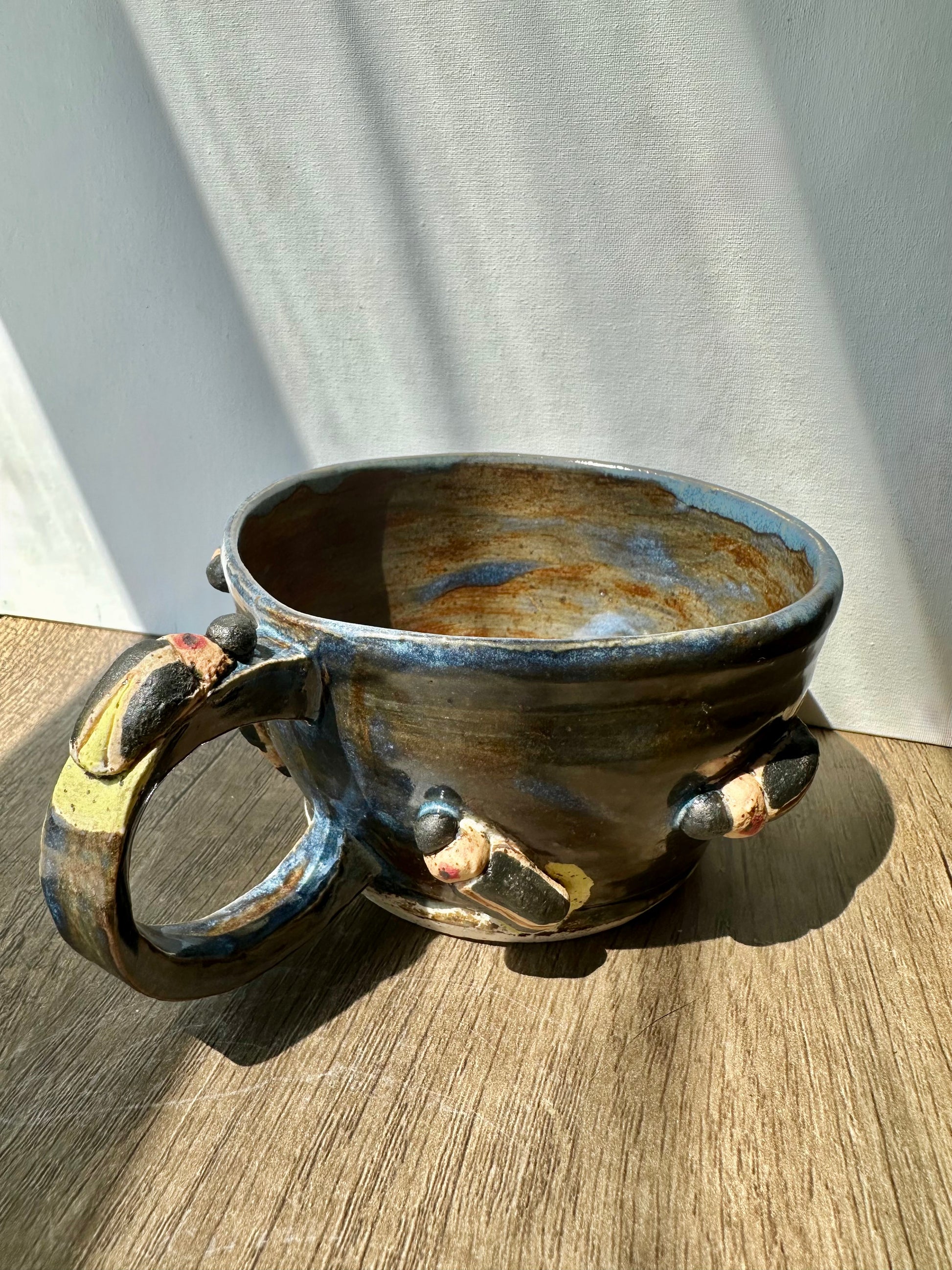 Bronze-colored mug with streaks of inky blue and sculpted fireflies.