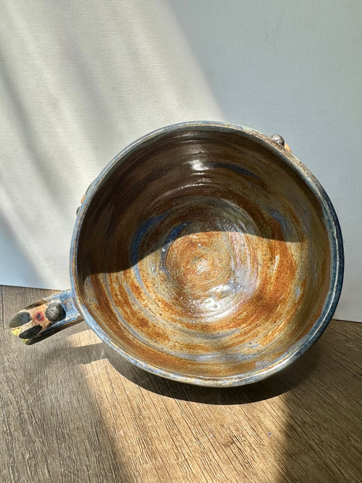 Interior of mug; bronze-colored with streaks of inky blue and sculpted firefly on the handle.