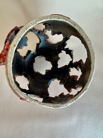 Interior of decorative ceramic sphere with maple leaf-shape cutouts viewed from the underside; interior is a very dark bronze glaze.