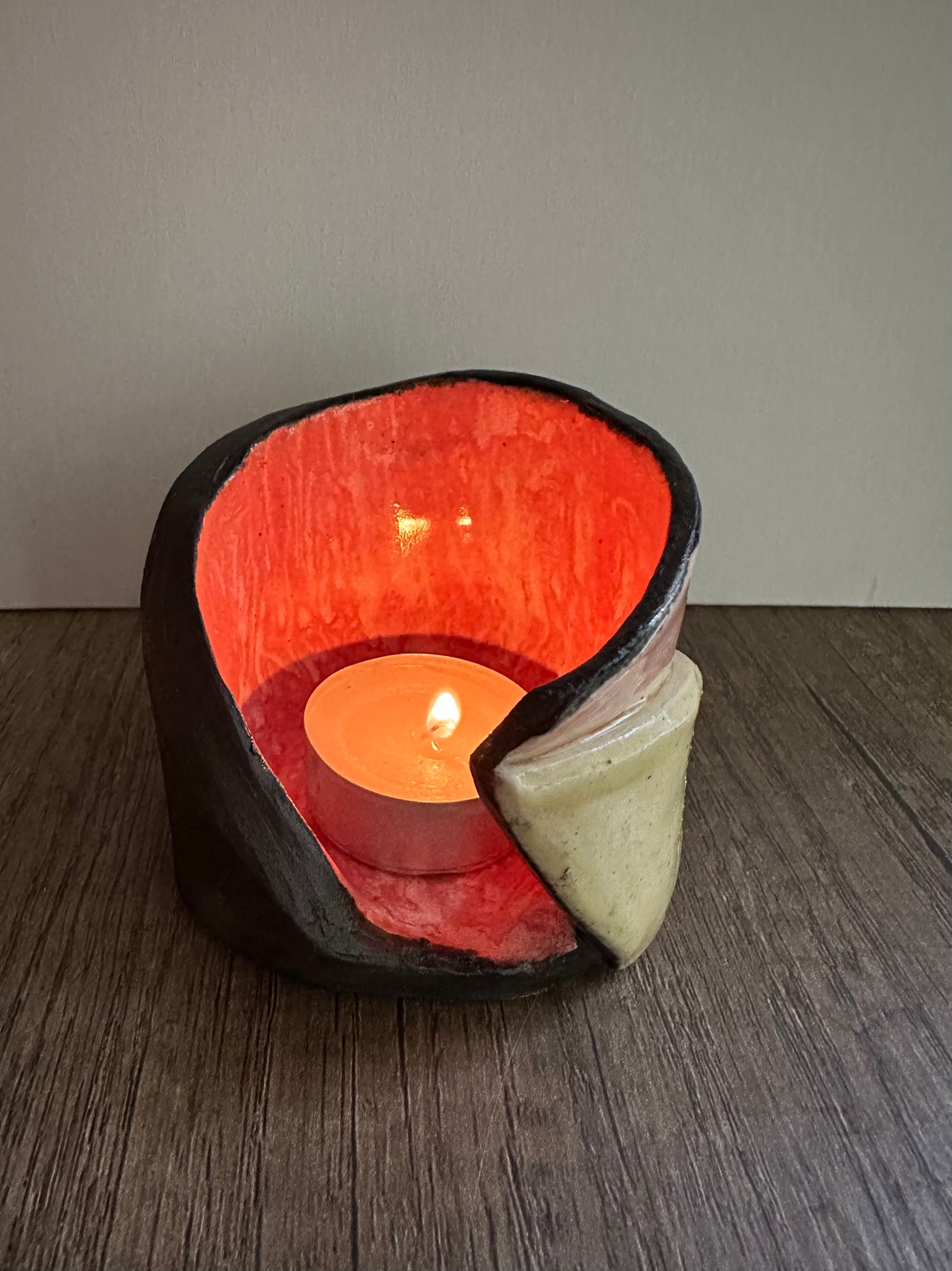 Ceramic multi-colored candle holder illuminated by a lit tea light.