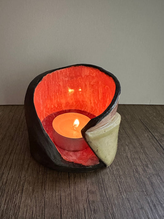 Ceramic multi-colored candle holder illuminated by a lit tea light.