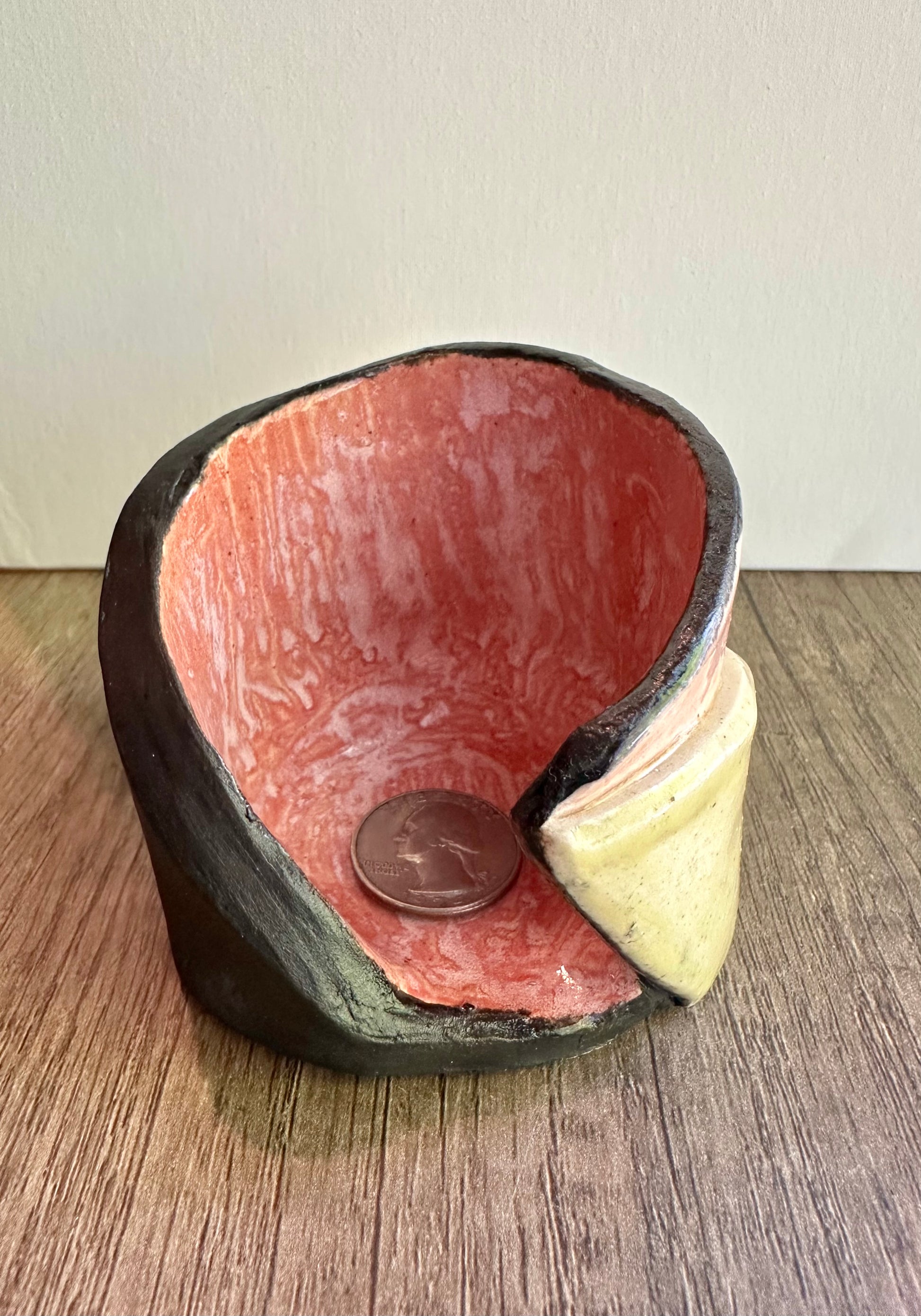 Front view of peachy interior of multi-colored votive with a quarter inside for scale reference.