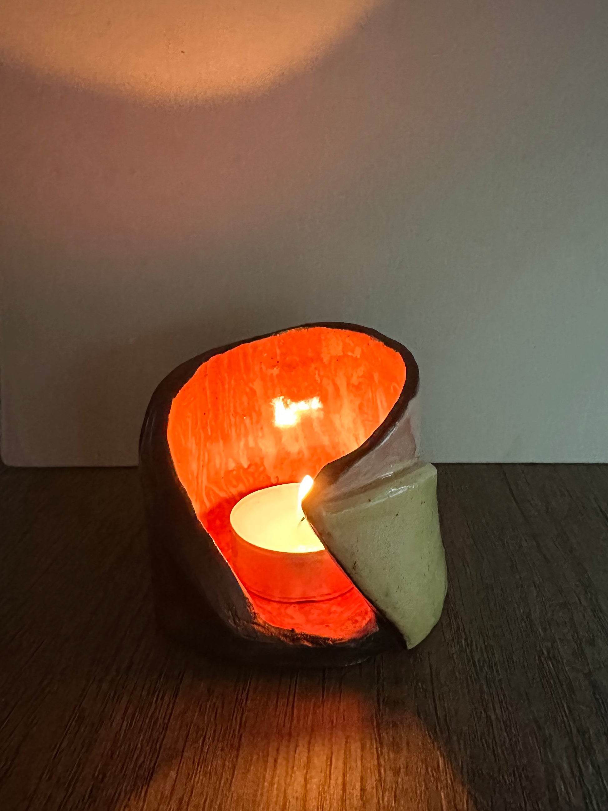 Ceramic multi-colored candle holder illuminated by a lit tea light.