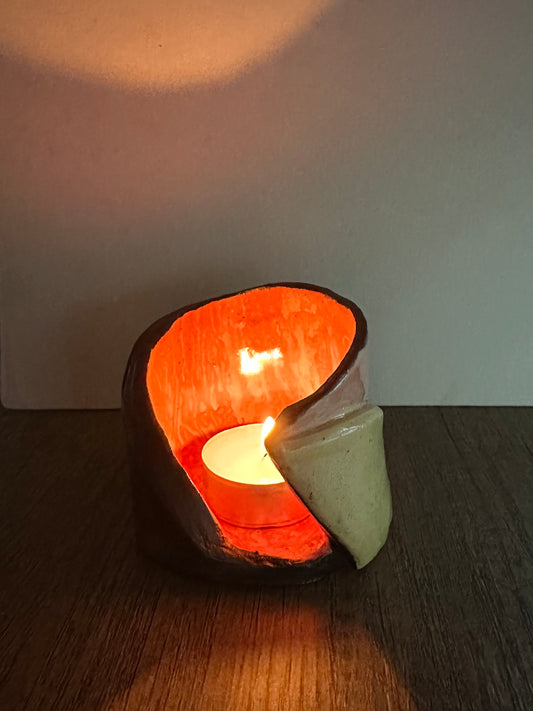 Ceramic multi-colored candle holder illuminated by a lit tea light.