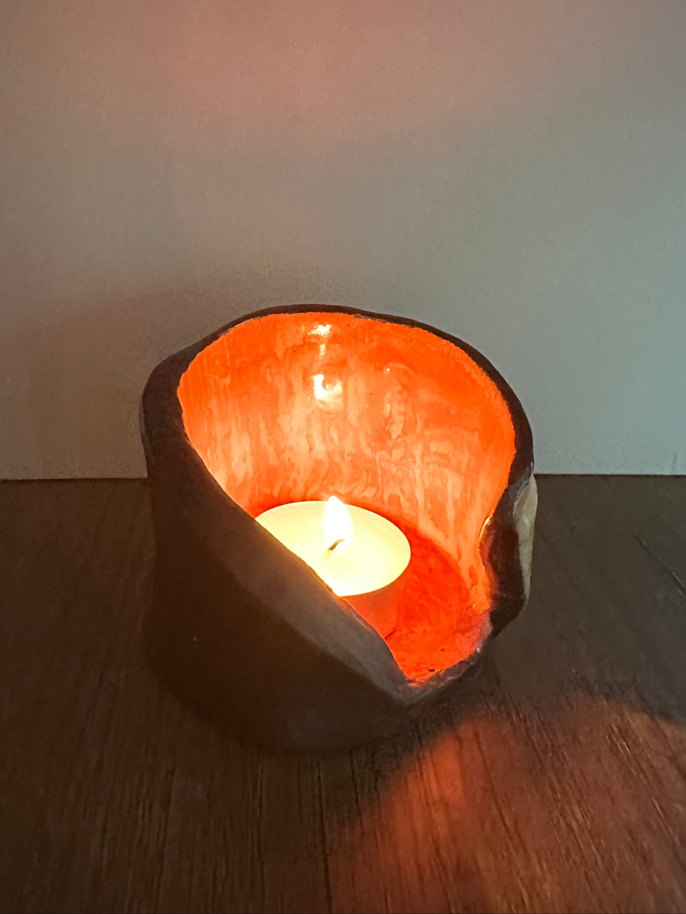 Ceramic multi-colored candle holder illuminated by a lit tea light.