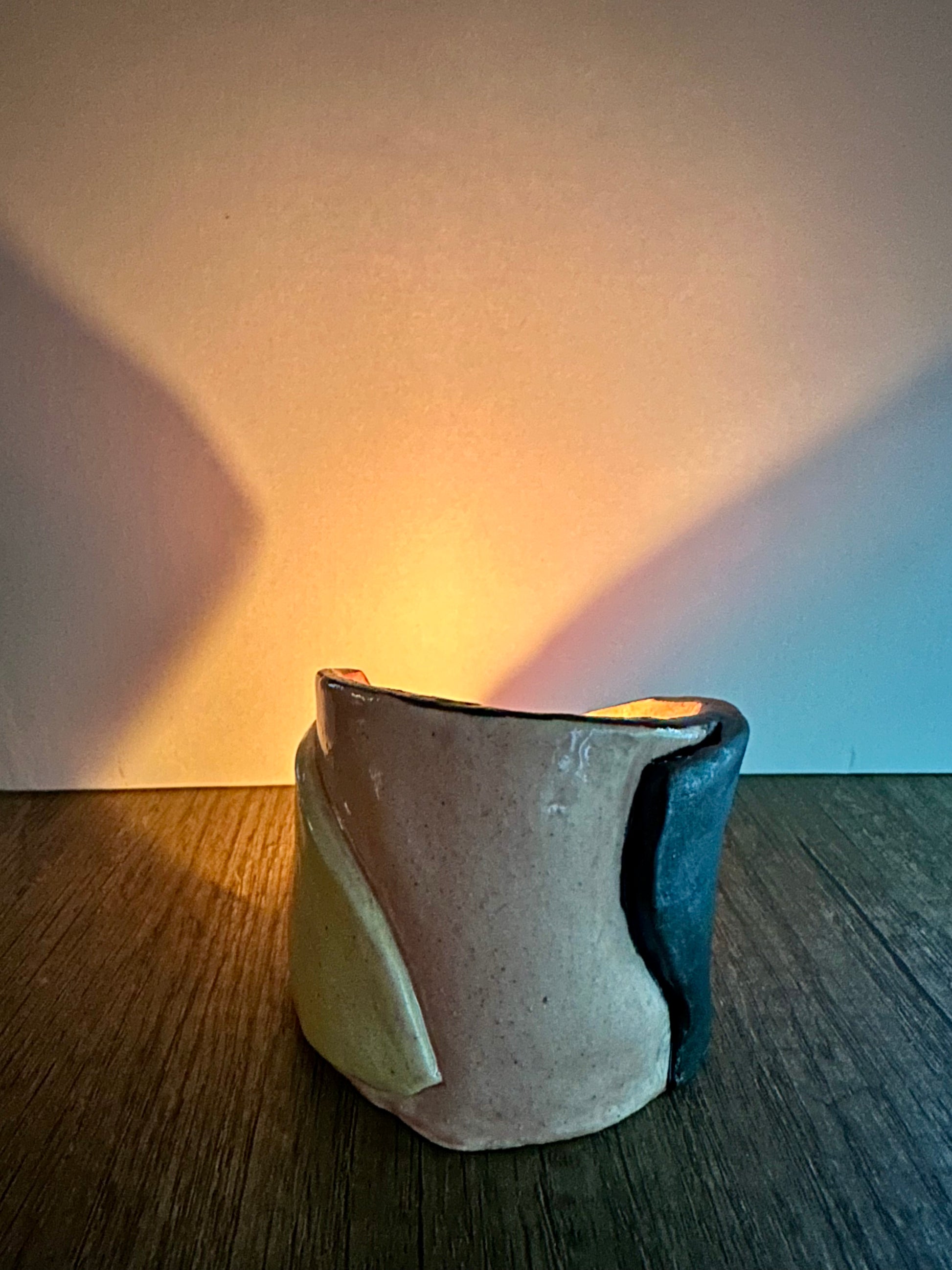 Ceramic multi-colored candle holder illuminated by a lit tea light.