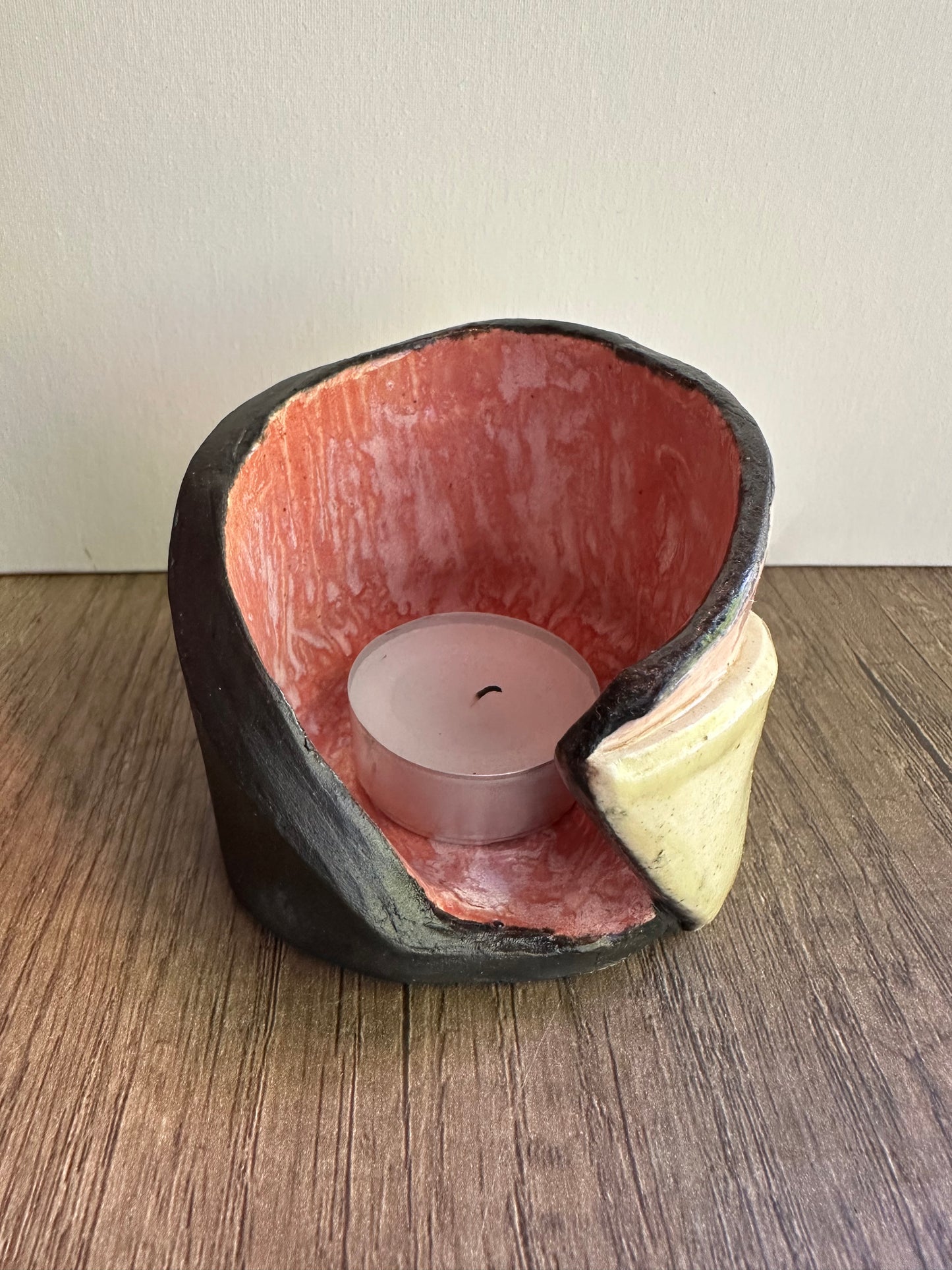 Ceramic multi-colored candle holder in neutral daylight with unlit tea light.