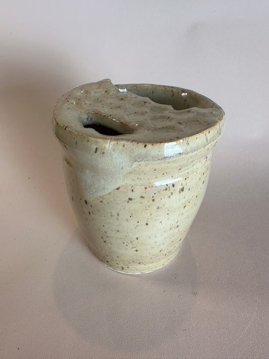 A beige speckled travel mug with half lid carved to look like a Dutch waffle cookie.