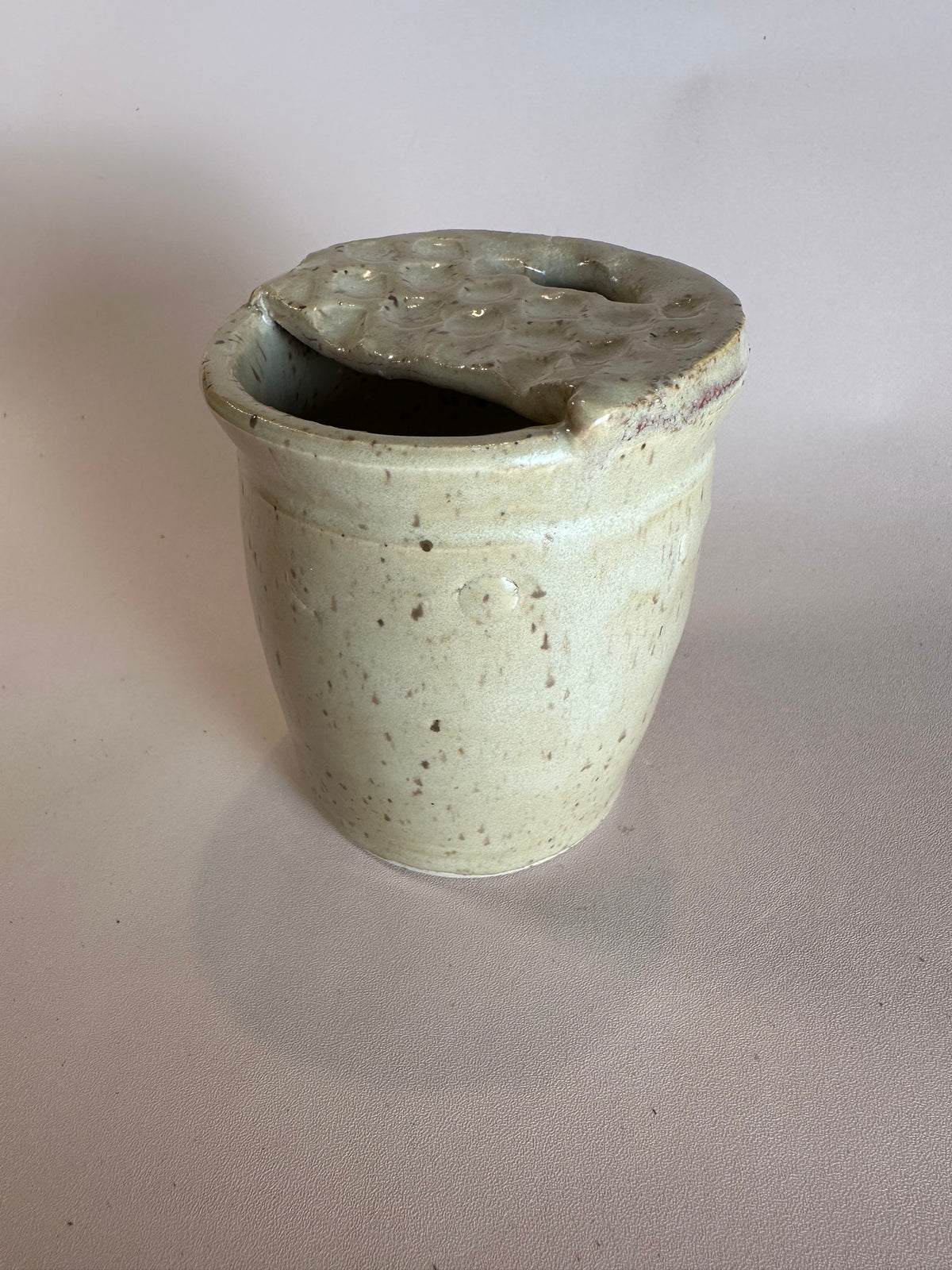 A beige speckled travel mug with half lid carved to look like a Dutch waffle cookie.