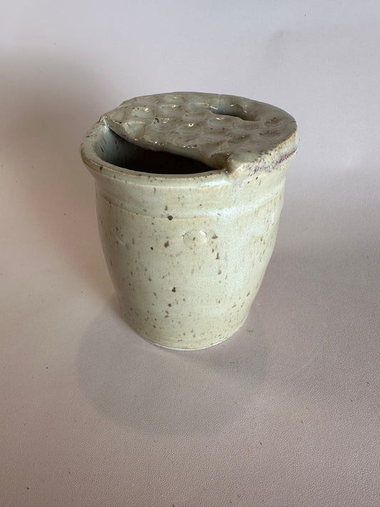 A beige speckled travel mug with half lid carved to look like a Dutch waffle cookie.