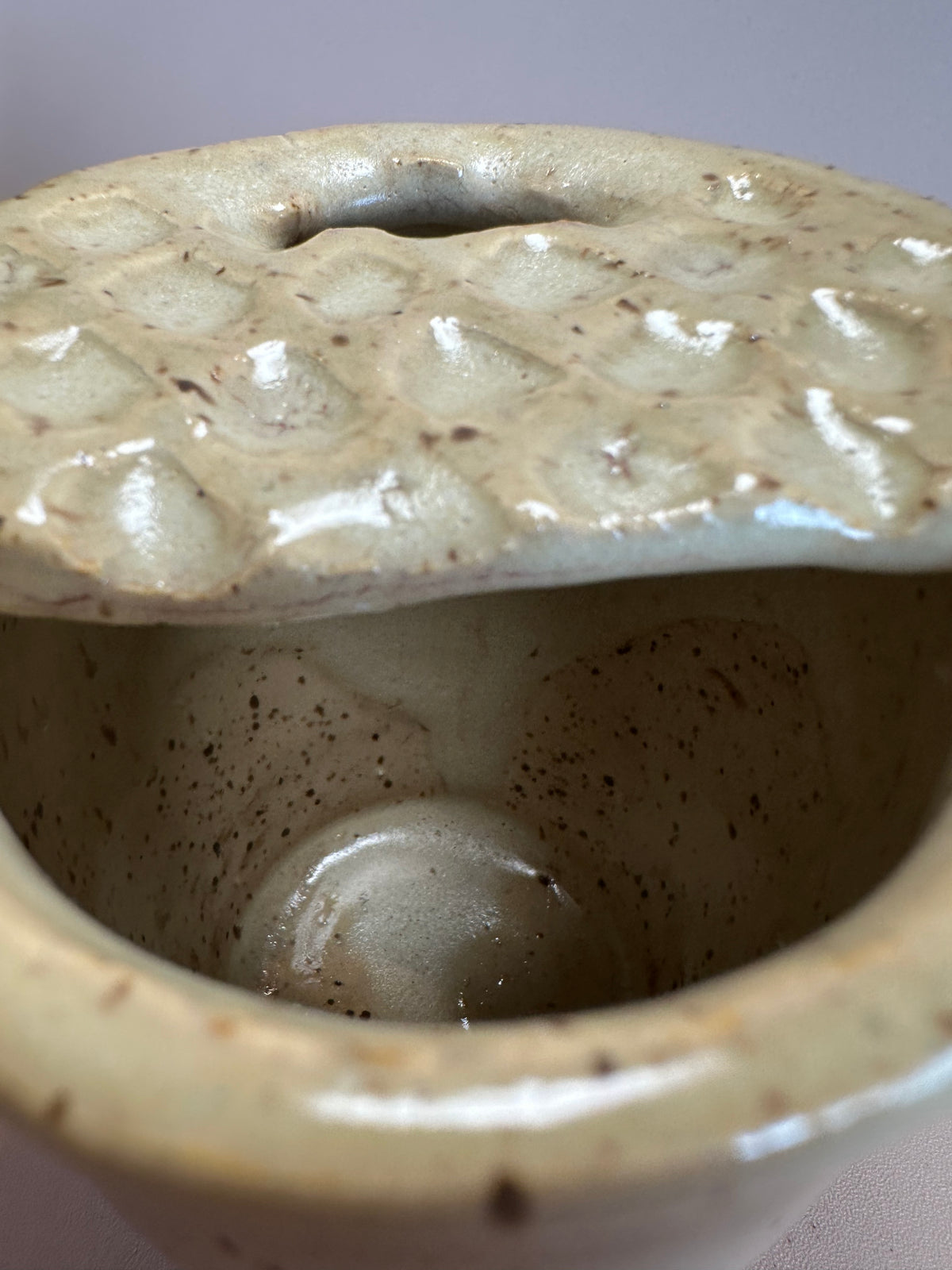 Interior of a beige speckled travel mug with half lid carved to look like a Dutch waffle cookie.