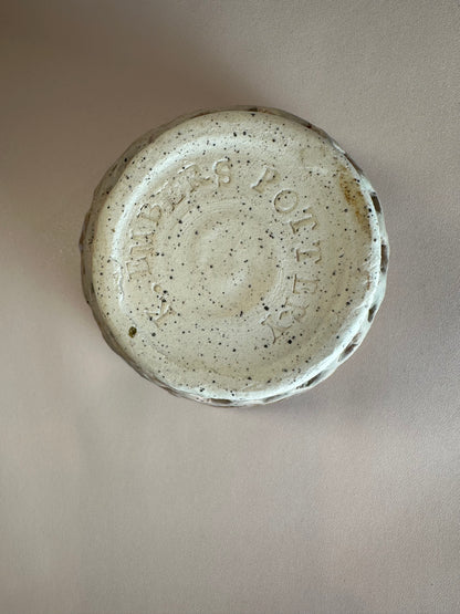 The bottom of a round ceramic bowl, showing a black-speckled white clay with and "K. Embers Pottery" stamped into the base.